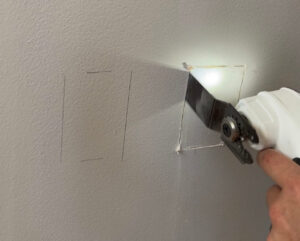 Cutting the traced lines of the outlet box out of the drywall by using my multi-tool.