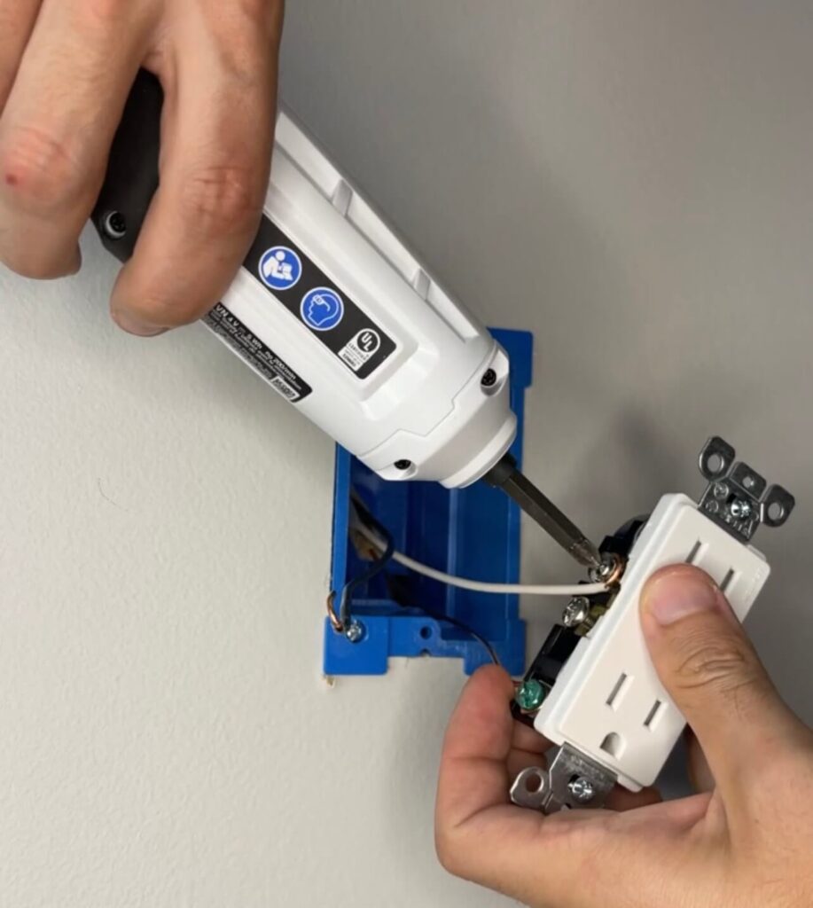 Using a screwdriver to hook the white wire to the silver screw on the outlet.